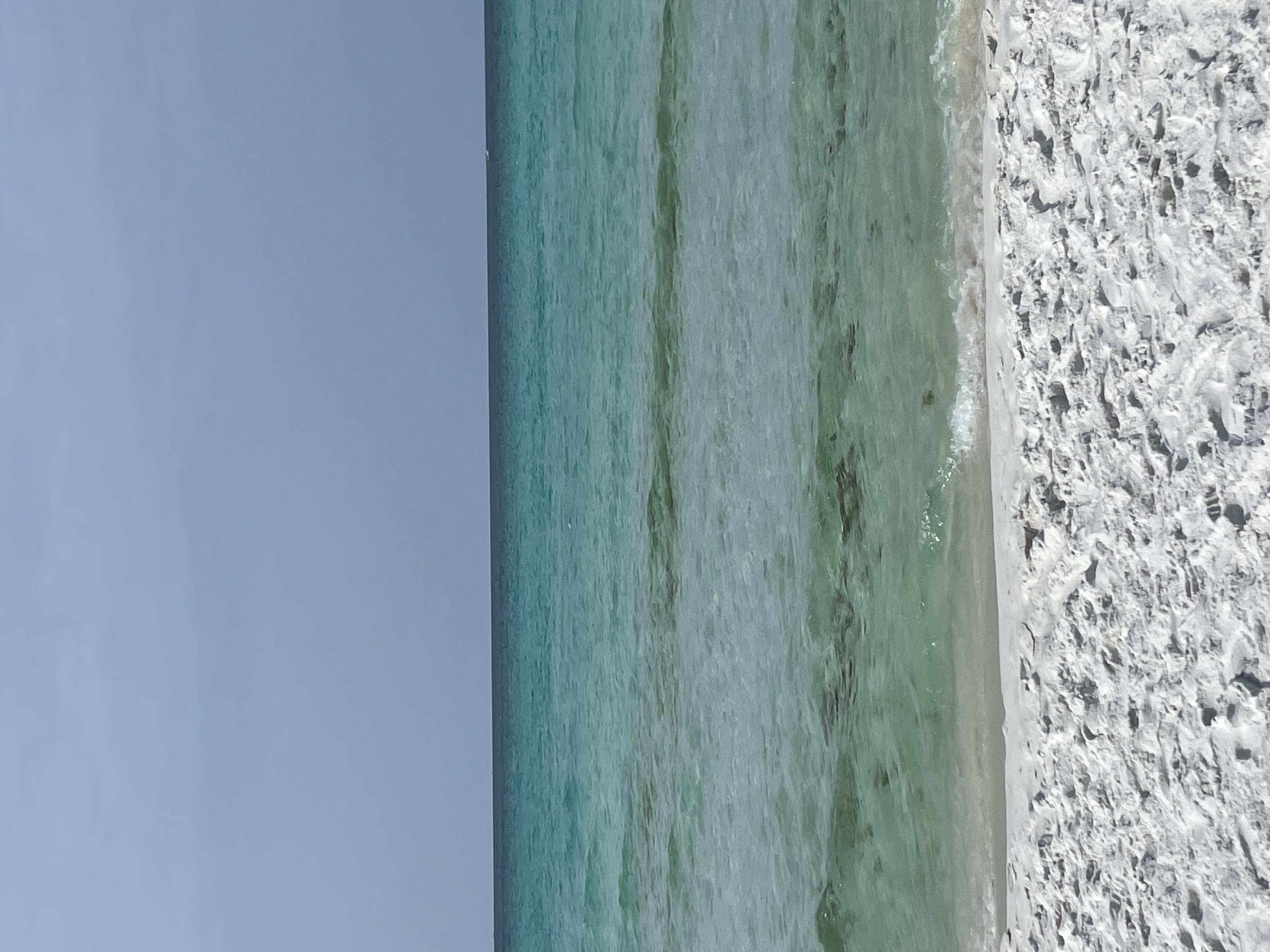 a picture of the shore of a beach on Destin. The water is blue-green and the sky is clear.