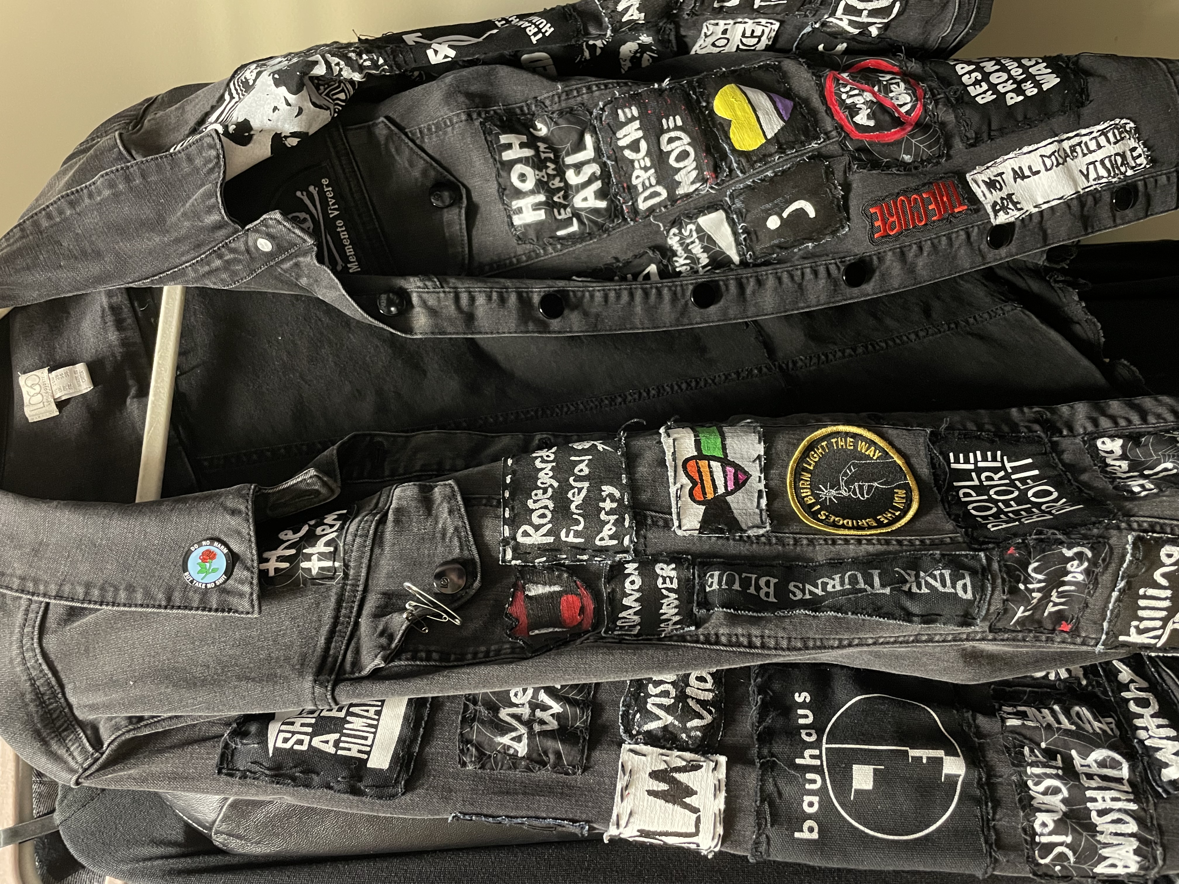 a black denim jacket with patches in various colors with slogans and bands on them. There is a pin on the collar that says,