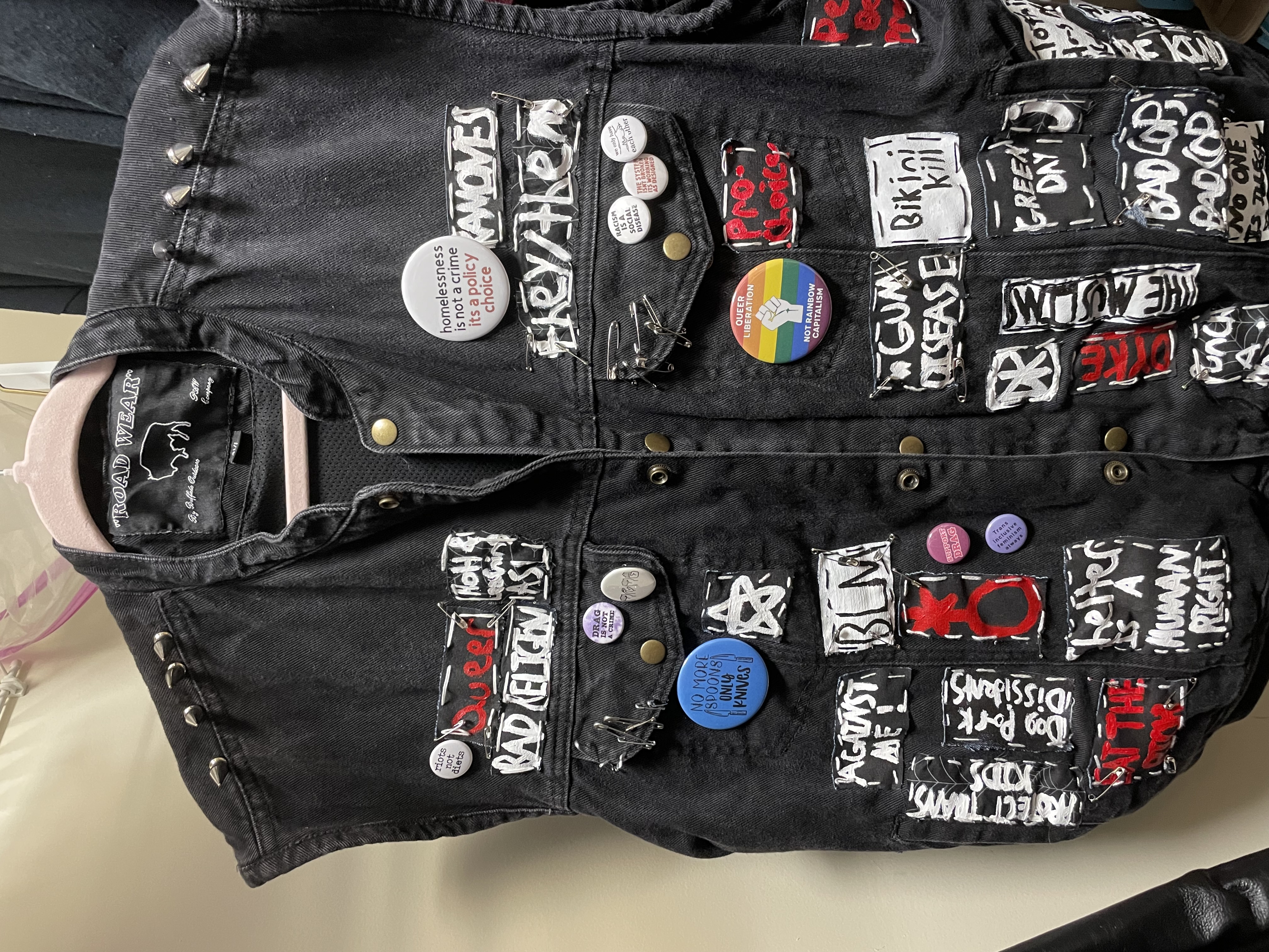 black denim vest with patches, spikes, safety pins, and button pins on it.